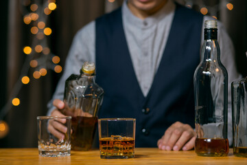 Waitress man standing pours whiskey into a glass 