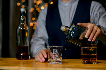 Waitress man standing pours whiskey into a glass 