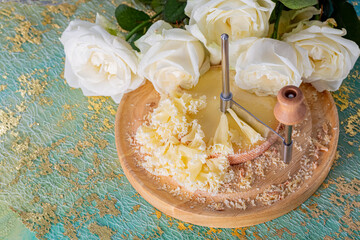 Scraper or knife for slicing and tasting tasty cheese chips on a green table. White roses. Closeup of rosettes Swiss cheese.