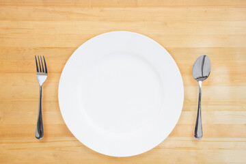 One blank white ceramic plate with a spoon and fork on a wooden floor or wooden table.