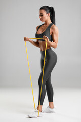 Fitness woman workout with resistance band isolated on gray background. Athletic girl doing...