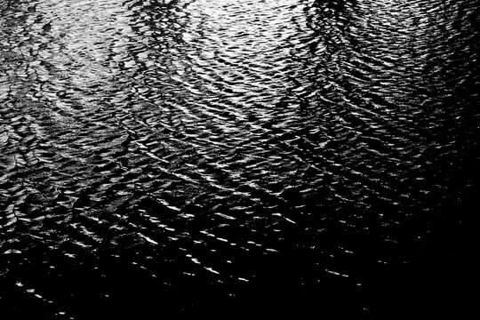 Black and white picture of water waves in the river, sea or ocean in the dark.