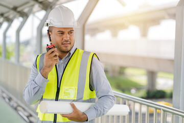 Portrait engineer handsome man or architect looking construction with the command of a radio. and white safety  helmet in construction site.