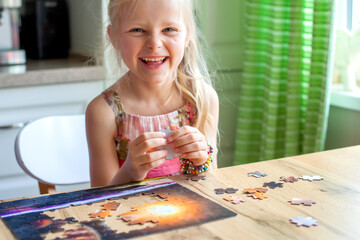 A girl sits at a table and collects a puzzle at home. she looks at the camera and laughs..Learning...