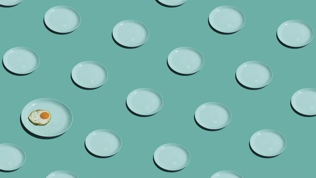 Pattern with lonely fried eggs and many empty plates animated on mint background. Plates move in different directions. 4K