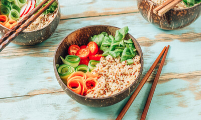Vegan Buddha bowl. Healthy meal quinoa, tomato, cucumber, carrot, radish, corn salad in coconut bowls on blue rustic background.