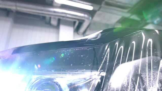 Close-up pan across the front of a new car as a clear paint protection film is applied.