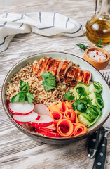 Healthy buddha bowl lunch with grilled chicken, quinoa, cucumber, radish, carrots on white wooden background.