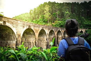 Young woman looks at the Demodara nine arches bridge over the tea plantation in the morning sunlight, the most visited sight of Ella town in Sri Lanka. 