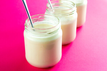 Three glasses of creamy yogurt on pink background