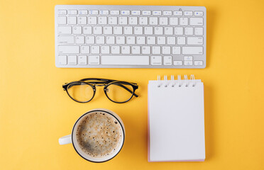 Home office workplace: cup of coffee, empty notebook, keyboard, tulip flowers on yellow background. Flat lay, top view. Work from home