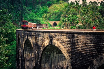 Vintage Train with observation car in motion over the world renowned nine arches bridge Demodara, Ella through beautiful lush green and tea estates towards the ella tunnel in the morning light