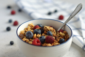 Oatmeal muesli with raspberries and blueberries in a white bowl with a blue border and a spoon on the background of a checkered towel on a light concrete background. Healthy food, healthy Breakfast.