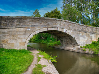 Sandstone Bridge 23 on a quiet, rural section of the Leeds to Liverpool Canal in Lancashire, UK. Taken on a sunny day with blue sky and white clouds in summer.