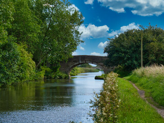 Fototapeta na wymiar Two bridges on a quiet, rural section of the Leeds to Liverpool Canal in Lancashire, UK. Taken on a sunny day with blue sky and white clouds in summer.
