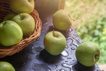 Green apples in drops of water on a black metal board on a background of green grass