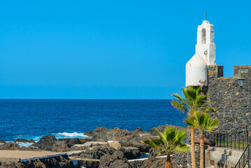 View on the ocean and volcanic rocks in the sea. Old wall with a cross. Calm ocean and blue sky
