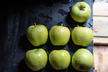 Green apples in drops of water on a black metal board on a background of green grass