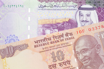 An orange, Indian ten rupee bill, close up with A colorful five riyal note from Saudi Arabia