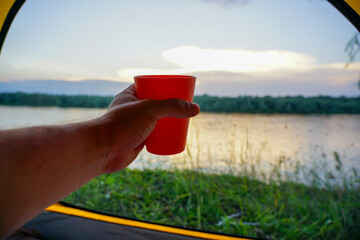 The hand from the tent holds a glass on the background of the river