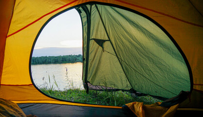 A tent with an open window stands on the banks of the river. From the open tent you can see the river