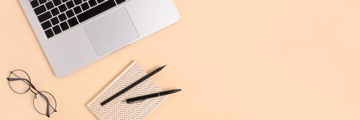 Office desk with laptop, glasses and notepad on a beige background. Banner with place for text.