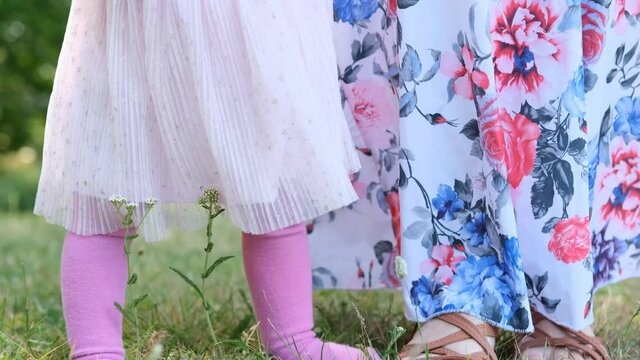 woman in a long dress, mom, teaches you to walk a little kid, a girl with blonde hair on grass in summer, concept of family summer vacation, outdoor games, first steps, child development