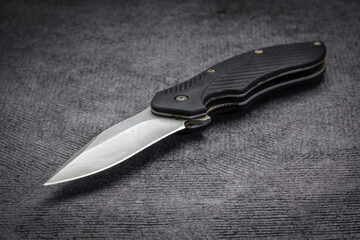 opened, used pocket knife with assisted opening on a black textured paper