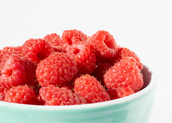 Fresh raspberries in ceramic bowl on white table. Close up photo with sunlight.