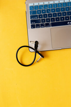Cable para instrumento musical al lado de un computador port&aacute;til sobre un fondo amarillo.