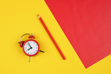 red alarm clock with a pencil on a red-yellow background