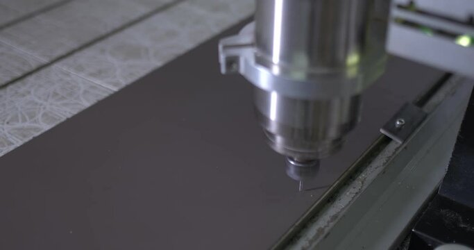 Drill is lowered into a sheet of plastic and begins to cut part of the caviar shavings. CNC milling plant. Close-up, top view.