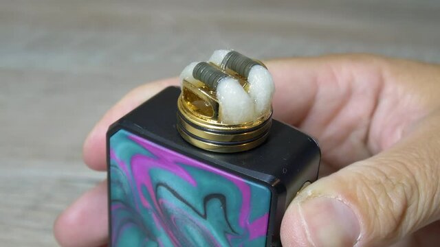Heating coils and cotton stripes full of e-liquid in rebuildable dripping atomizer or RDA for vaping. Vapor clouds spread everywhere. 4K macro video with selective focus.