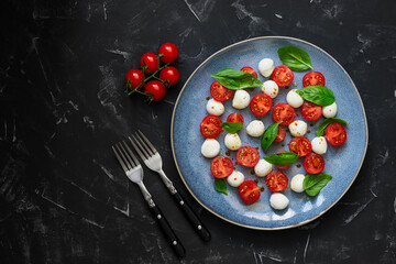 Caprese salad. Traditional Italian dish: mozzarella, tomato, basil on a black stone background. Top view, flat lay, copy space.