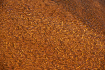 Colorful nature background of yellow red clay bottom. Natural texture of multicolored clay in clear water of mountain creek. Red yellow sandy bottom of mountain river. Full frame of ripples on water.