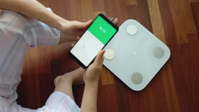 Crop woman using digital weight scales and smartphone application