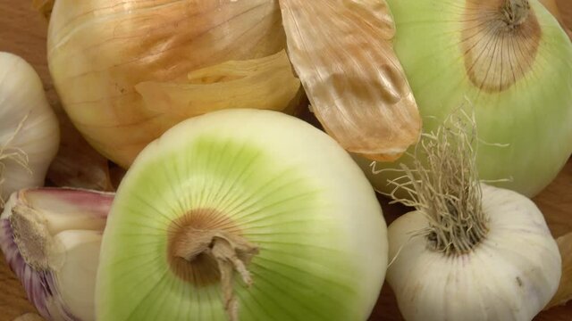 Yellow onions, garlic and dry onion skin are laid out on a wooden board