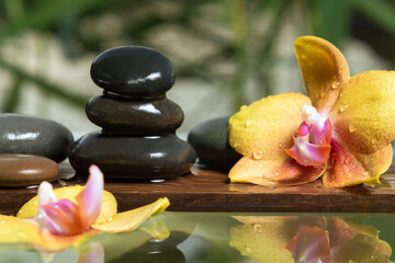 Black zen stones and yellow orchids on a wooden plank on the surface of the water. SPA, relaxation, meditation concept