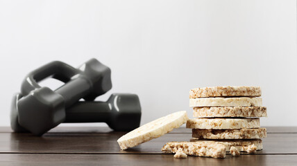 Rice and buckwheat cakes on a wood table. Dumbbells on a white background, healthy lifestyle.
