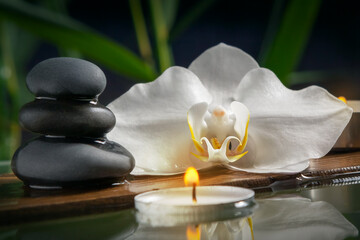 Fototapeta na wymiar Black zen stones,candles and white orchids on a wooden plank on the surface of the water. SPA, relaxation, meditation concept