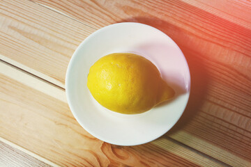 One lemon on a white plate on the table.