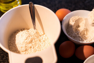 White bowls filled with flour and eggs and oil on top of the kitchen marble. Preparation for making a homemade cake in home.