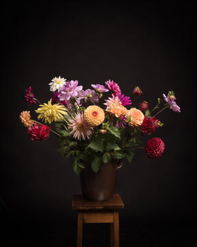 Studio still life of flower arrangement of colorful dahlias in vase in classic painterly style