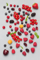 Still life of multi-colored berries on gray background. Red currants, raspberries red and yellow, blueberries green mint.