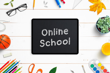 Online school on tablet surrounded by school supplies on white wooden desk. Top view, flat lay composition. Classes at the time of virus epidemic concept