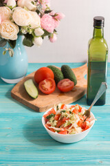 Vegetarian salad with fresh vegetables and olive oil on a blue wooden table. A bouquet of flowers in the background. Light summer dinner