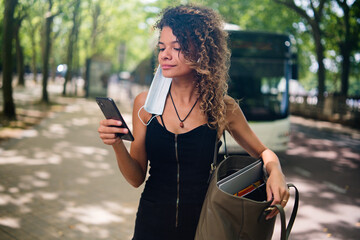 Young woman wearing a protective mask in a wrong manner and looking at her phone