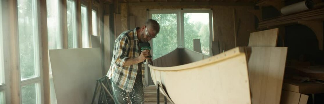 Mid 50s Caucasian male building a canoe in his workshop, using milling tool. Boat making hobby, small business owner. Shot on RED Dragon