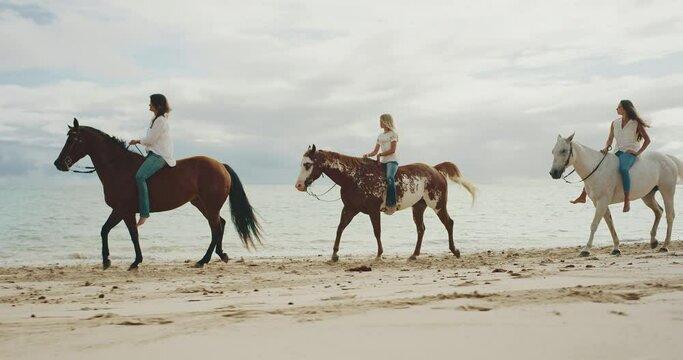 Horseback riding on the beach at sunrise, three friends riding down the beach, cinematic slow motion