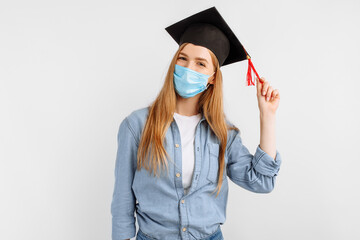 dreamy, brooding girl-a graduate student, with a medical mask on her face and a graduation cap on her head, on a white background. Graduation, distance education, coronavirus